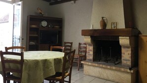 A dining area with a table set for four, a fireplace, and a bookshelf with various items. - Cozy house near Blois, pets allowed, parking (Chailles)
