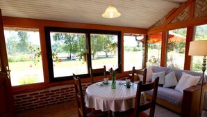 A cozy room with a brick wall, a wooden ceiling, and large windows offering a view of a garden. - Charming Restored Barn with Tennis, Near Loire Castles & ZooParc de Beauval, Pet-Friendly, Sleeps 3 (Cheverny)