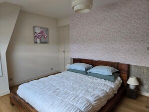 A bedroom with a wooden bed, a nightstand with a lamp, a floral painting on the wall, and a patterned wallpaper. - Charming Restored Barn with Tennis, Near Loire Castles & ZooParc de Beauval, Pet-Friendly, Sleeps 3 (Cheverny)