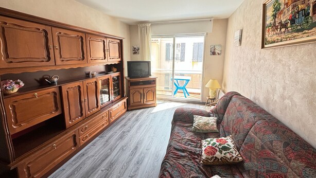A living room with wooden cabinets, a television, a patterned sofa, and a balcony with a blue chair.
