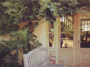 A wooden bench under a tree with a door and window in the background. - Charming 3-Bedroom Cottage in Sologne Forest with Modern Amenities and Scenic Views (Theillay)