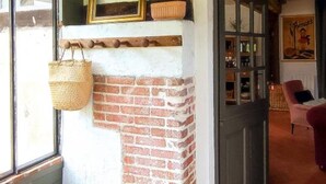 Une pièce avec une cheminée en briques, un tableau encadré au-dessus, et un panier en osier accroché au mur.