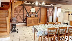 A rustic kitchen with wooden beams, a brick wall, and a dining area with a table and chairs. - Charming cottage with garden, pets allowed (Fresnes)