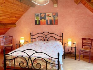 A bedroom with a sloped ceiling, a metal bed frame, two bedside tables with lamps, and a painting above the bed. - Charming cottage with garden, pets allowed (Fresnes)