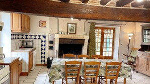 A cozy kitchen with a dining table set for four, wooden cabinets, a tiled backsplash, and a fireplace. - Charming cottage with garden, pets allowed (Fresnes)
