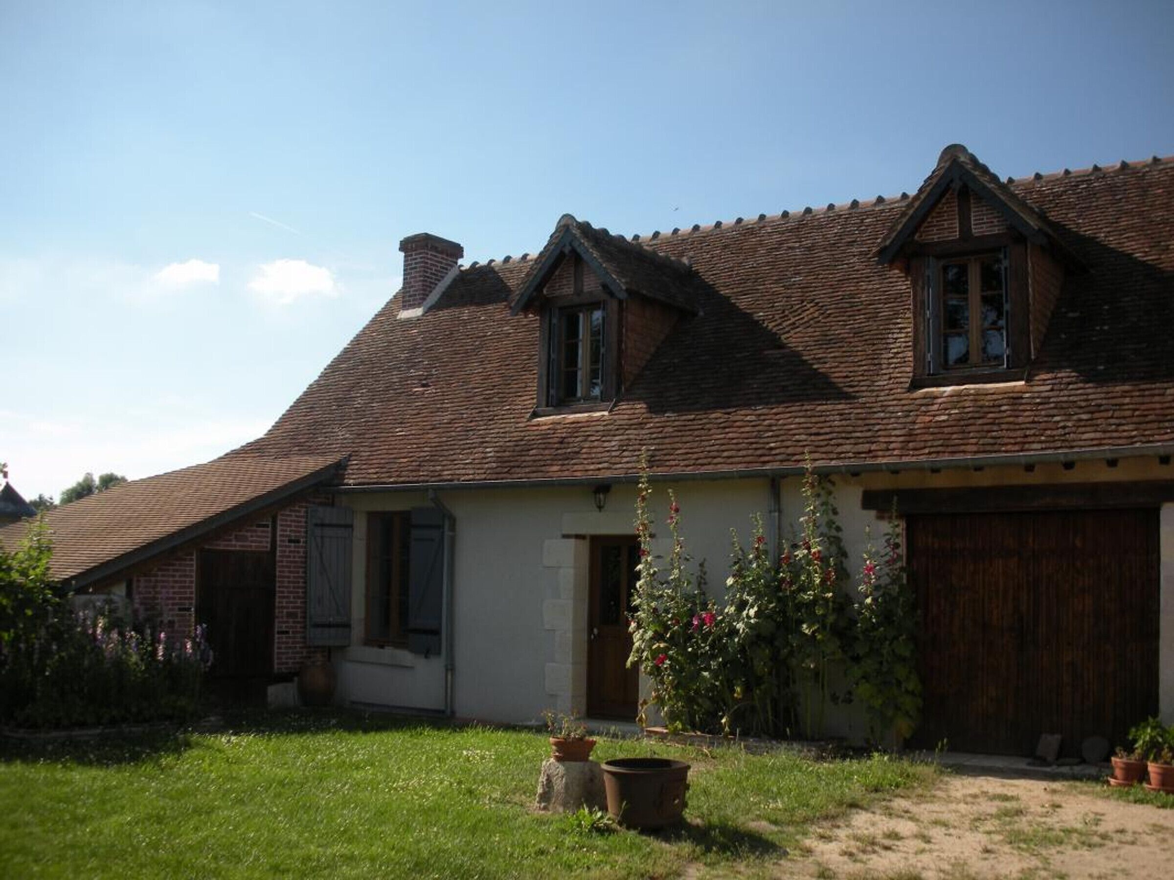 A traditional house with a sloped roof, a chimney, and a front door. There are potted plants in the front yard.