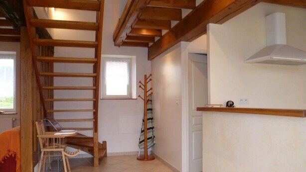 Una habitación con una escalera de madera, una silla, un perchero y una puerta blanca.