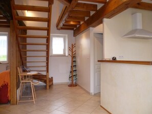 Una habitación con una escalera de madera, una silla, un perchero y una puerta blanca.