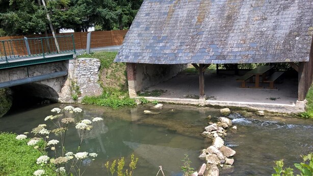 Een rustieke stenen brug over een kalme beek, met een klein houten gebouwtje aan de rechterkant.