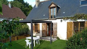 Een huis met een overdekte patio, een witte tafel en stoelen, en een verzorgd gazon.