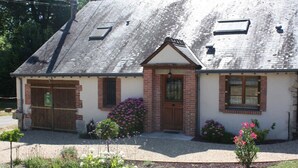 Een tweelaags huis met een schuin dak, een voortuin en een kleine tuin met bloemen en struiken.