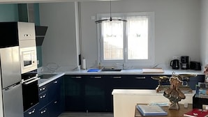 A modern kitchen with dark blue cabinets, a white countertop, a built-in oven, and a window with a view of the outside.