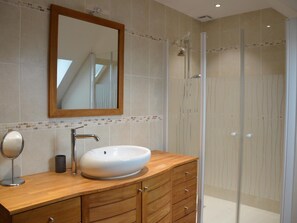 Une salle de bain avec un meuble-lavabo en bois, un grand miroir, un lavabo blanc et une cabine de douche en verre.