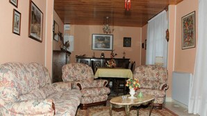 A living room with floral-patterned sofas, a wooden ceiling, a dining table with a yellow tablecloth, and a patterned rug. - Charming Cottage with Private Garden, Terrace & Garage near Loire Castles (Huisseau-sur-Cosson)