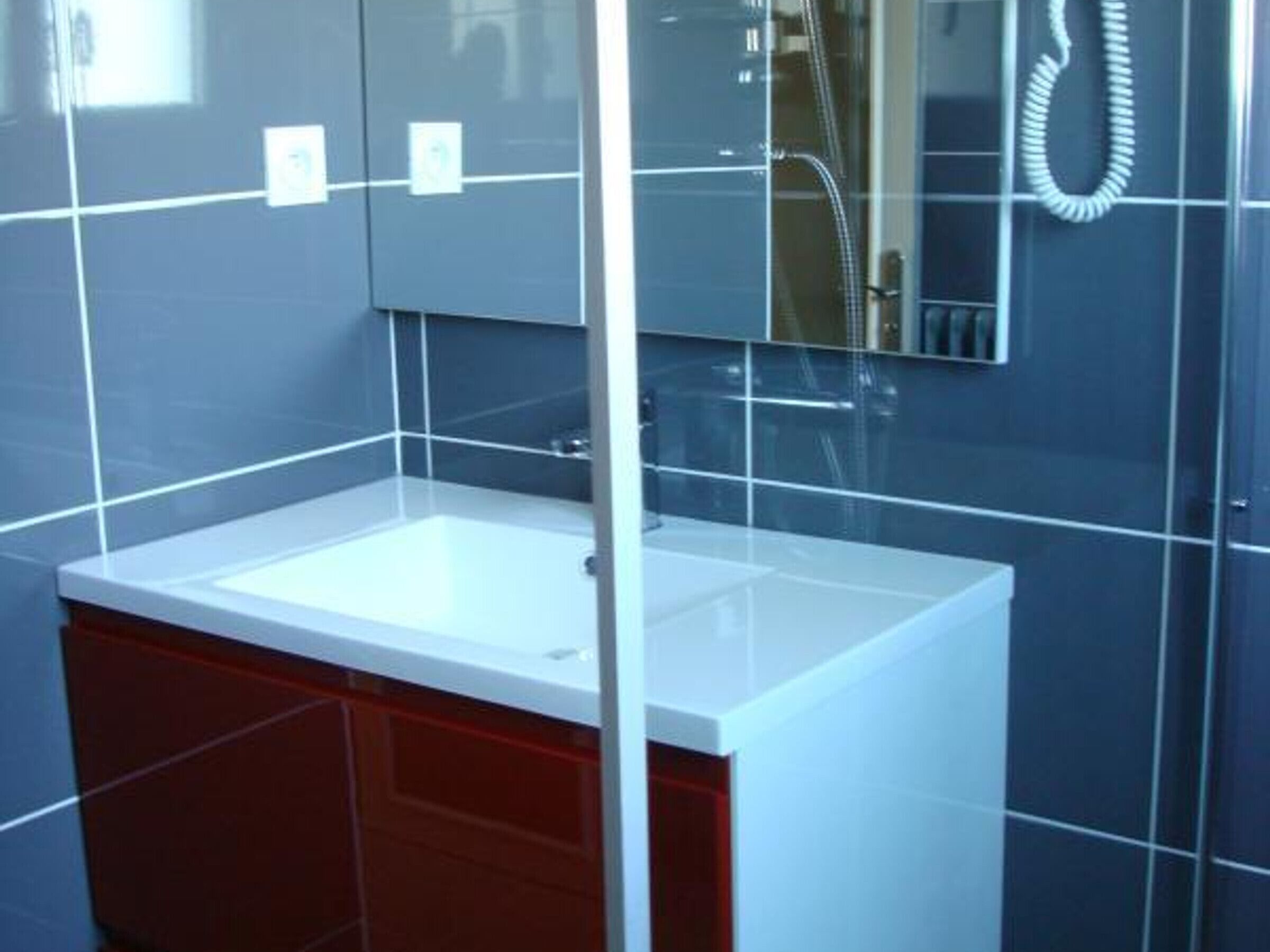 Une salle de bain avec un lavabo blanc, des meubles rouges et un miroir.