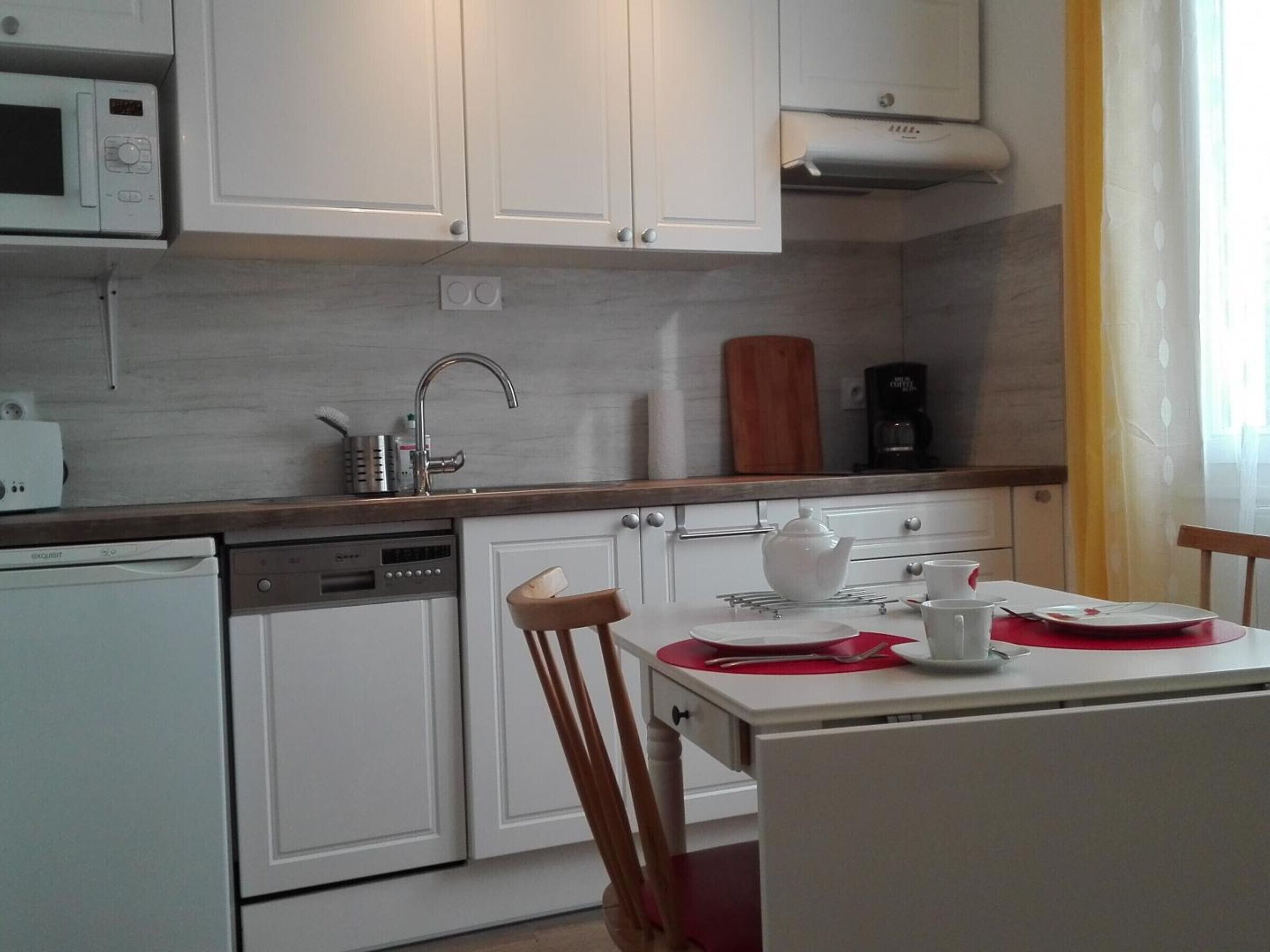 Una cocina compacta con armarios blancos, microondas, cafetera y una mesa de comedor con sillas.