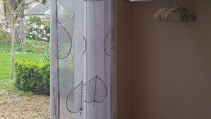 A room with a window featuring a leaf-patterned curtain, a wooden shelf with a towel, and a view of a garden and houses outside. - Cozy studio with shared garden and parking, ideal for couples facing Pontlevoy Abbey (Pontlevoy)