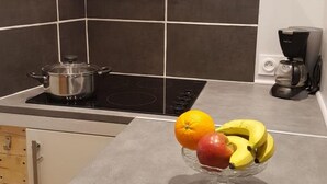 A kitchen with a stove, a coffee maker, and a bowl of fruit on the counter. - Cozy studio with shared garden and parking, ideal for couples facing Pontlevoy Abbey (Pontlevoy)