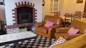 Un salón con suelo de cuadros, una chimenea con marco de ladrillo, sofás de cuero con cojines rosados, y una zona de comedor con sillas de madera y una mesa.