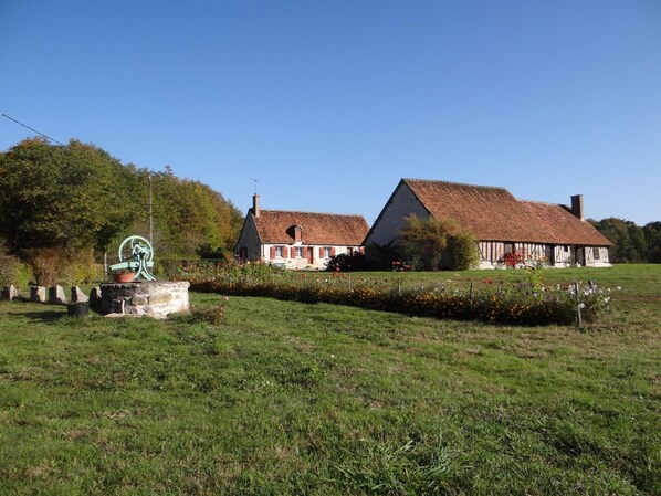 A rural setting with two traditional houses, a stone well, and a green pump.