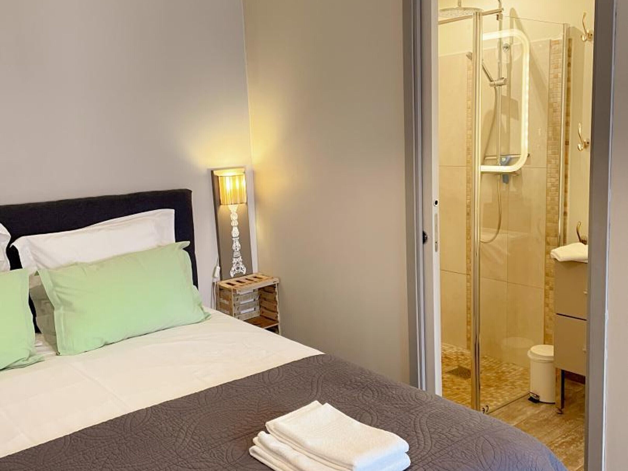 A hotel room with a bed, a nightstand with a lamp, and a glass-enclosed shower area.