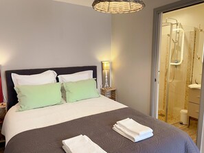 Une chambre d’hôtel avec un lit, des oreillers, une lampe de chevet, une salle de bain avec douche et une serviette sur le lit.