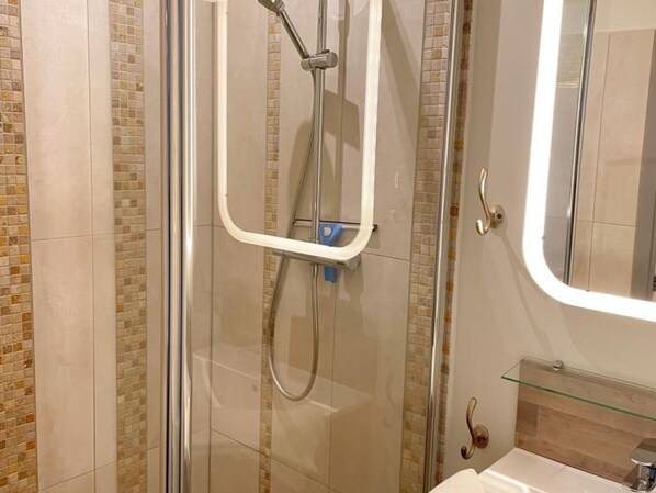 Une douche avec une porte en verre, une étagère en verre au-dessus du lavabo et un miroir au mur.