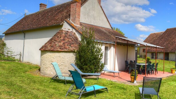 Uma casa com telhado em telhas, varanda coberta com móveis de exterior e um pequeno jardim.