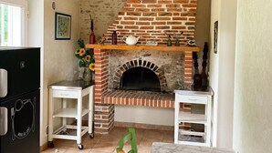 Uma cozinha com lareira de tijolos, armários brancos e uma pequena mesa com um vaso de girassóis.