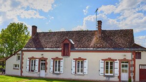 Um edifício de dois andares com telhado inclinado, chaminés de tijolos vermelhos e janelas emolduradas de branco com persianas.