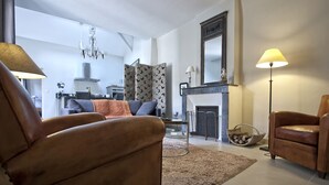 Een woonkamer met een open haard, een bank, een stoel en een lamp.