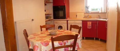 Una cocina compacta con armarios rojos, una mesa de comedor con mantel floreado y electrodomésticos básicos.