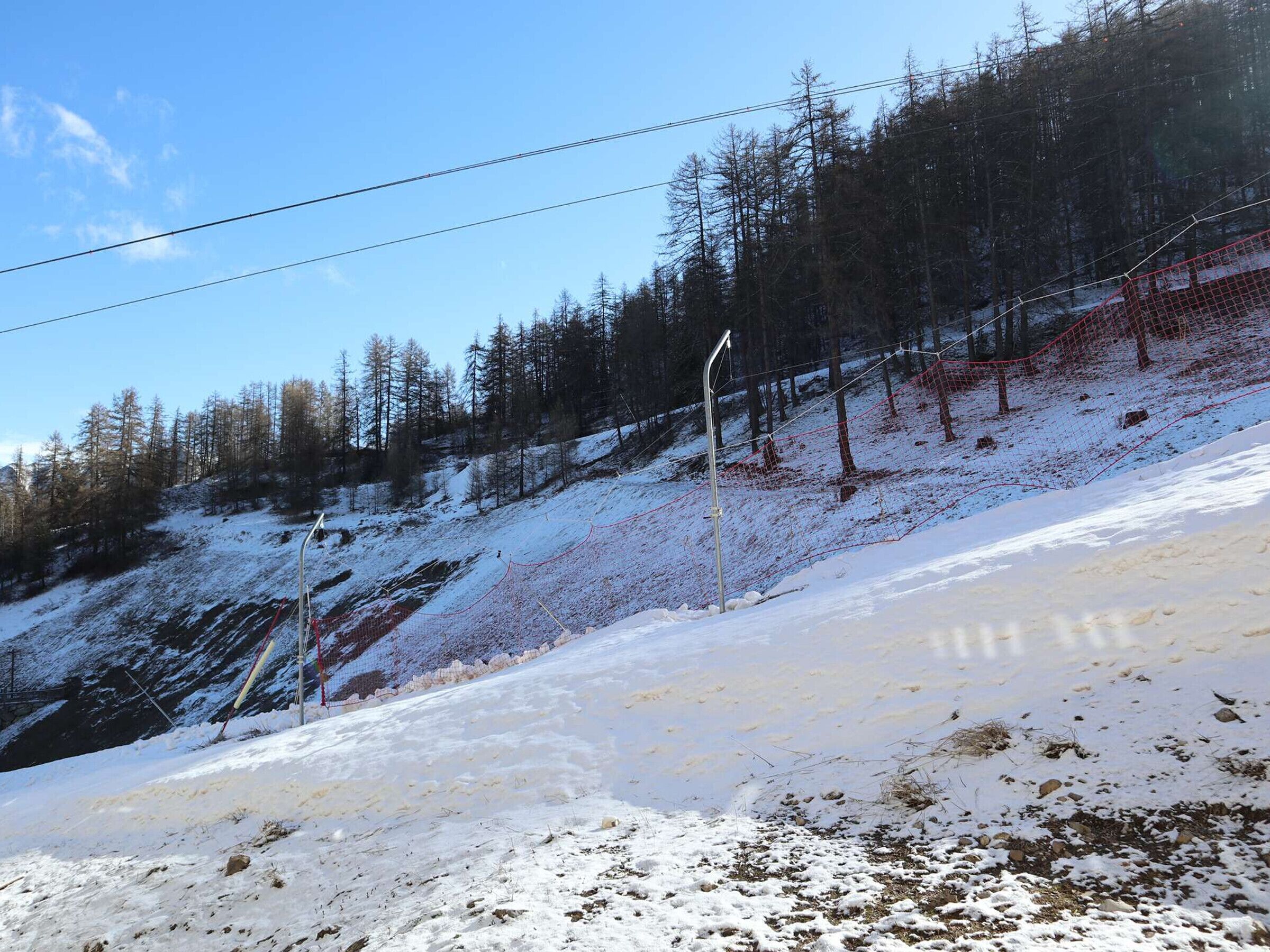 A snowy ski slope with a fence and trees in the background.