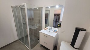 Ein modernes Badezimmer mit Duschkabine aus Glas, einem weißen Waschtisch mit Spiegel und einem schwarzen Mülleimer.