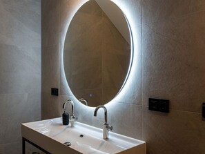A bathroom with a white sink, two faucets, a round mirror, and a soap dispenser.