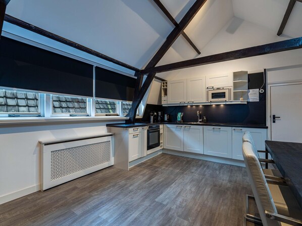 A modern kitchen with white cabinets, a black countertop, and a built-in oven. There is a window with a view of the roof and a radiator on the floor. - Beautiful Apartment on the First Floor Abcoude (Abcoude)