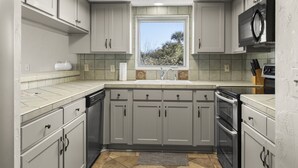 A modern kitchen with grey cabinets, a stainless steel oven, and a window providing natural light. - Ground Floor Condo Nestled Against The Dunes! (St. Augustine)