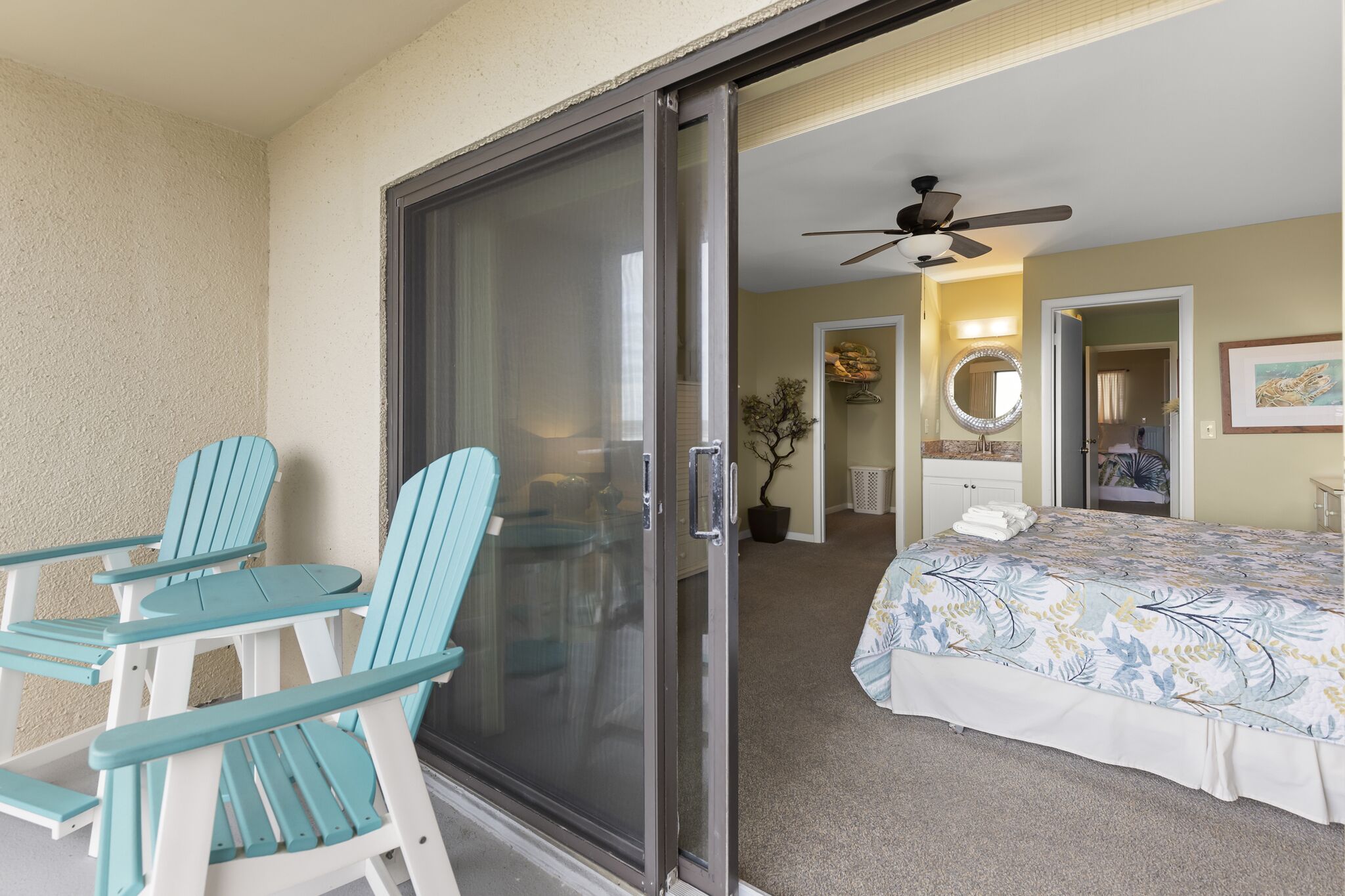 Une chambre avec un lit, un ventilateur de plafond, une porte-fenêtre coulissante et une petite table avec des chaises.