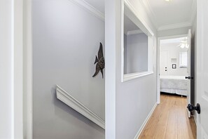 Een hal met een witte muur, decoratieve viskunst aan de wand, een witte deur met een zwarte deurklink, en een houten vloer.