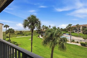 A view of a resort with a pool, palm trees, and a beach in the background.