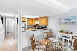 A modern kitchen with wooden cabinets, a built-in microwave, and a dining area with a glass table and wicker chairs. - Updated Oceanfront Condo With Two Private Balconies! (St. Augustine)