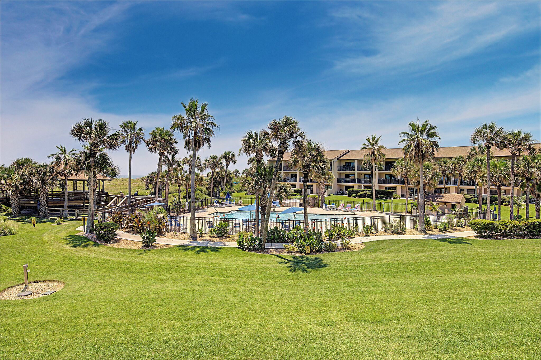 Un resort con piscina, palmeras y un edificio con balcones.