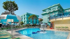 A swimming pool with lounge chairs and a water fountain, surrounded by buildings with a modern design.