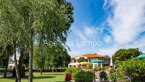 A sunny outdoor area with a grassy lawn, a stroller, and a building with a red roof.
