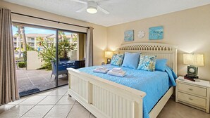 Une chambre avec un lit, une table de chevet, un ventilateur de plafond et une vue sur l’extérieur.