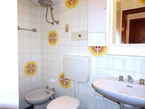 A bathroom with white tiles, a toilet, a bidet, a sink, and a shower with a curved pipe. - Apartment in Caorle Near Sandy Beaches (Caorle)