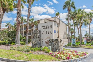 Schild für Ocean Villas mit Steinsockel und einem Gebäude im Hintergrund.