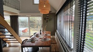 A dining area with a wooden table set for four, a hanging light fixture, and a view through a window with blinds. - Family Home Near Lake, Beach and Dunes (Noordwijkerhout)