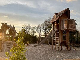 Un parque infantil con estructuras de madera, que incluyen un tobogán y una escalera de escalada.