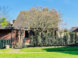 A brick house with a tiled roof, surrounded by a well-maintained lawn and a hedge.